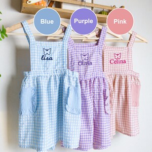 May include: Three gingham aprons with butterfly embroidery and personalized names. The aprons are blue, purple, and pink. The names are Lisa, Olivia, and Celina.