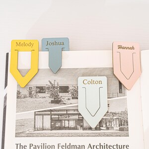 May include: Four personalized wooden bookmarks with gold lettering. The bookmarks are yellow, blue, light blue, and pink. The names on the bookmarks are Melody, Joshua, Colton, and Hannah.