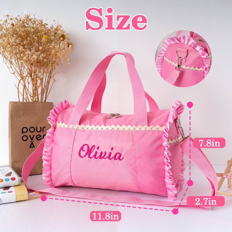 May include: Pink duffel bag with the name "Olivia" embroidered on the front. The bag has a ruffled trim, lace detailing, and a detachable shoulder strap. Dimensions are 11.8 inches long, 7.8 inches high, and 2.7 inches wide.