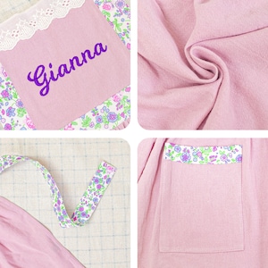以下が含まれることがあります： 紫色の「Gianna」の刺繍が入った、明るいピンク色のパーソナライズされたベビーブランケット。ブランケットは、花柄のトリムとマッチするリボンが特徴です。デザインには、花のトリムとレースのボーダーが付いたポケットが含まれています。