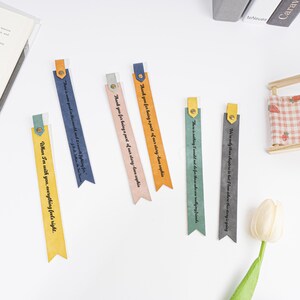 Puede incluir: Seis marcap&aacute;ginas coloridos con diferentes citas impresas en ellos. Los marcap&aacute;ginas est&aacute;n hechos de un material suave y texturizado y tienen una combinaci&oacute;n de colores amarillo, azul, rosa, verde y gris.