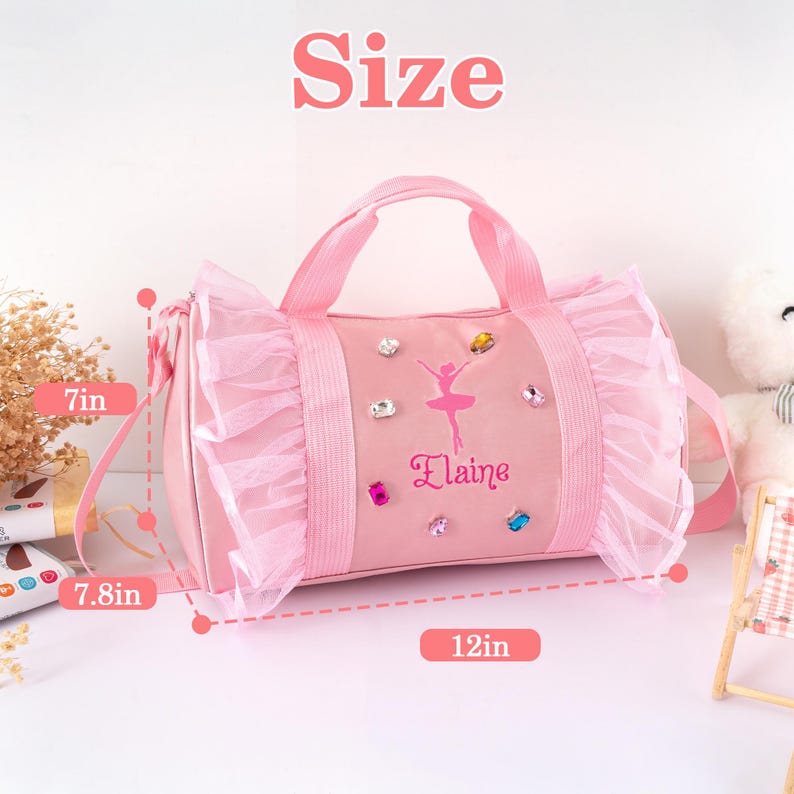 Peut inclure: Sac de ballet rose avec un graphisme de ballerine et le nom "Elaine". Le sac mesure 30.5 cm de long, 17.8 cm de haut et 19.8 cm de large. Il pr&eacute;sente une garniture &agrave; volants et des bijoux d&eacute;coratifs.