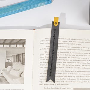 Puede incluir: Un marcap&aacute;ginas de cuero negro con una leng&uuml;eta de cuero amarillo. El marcap&aacute;ginas tiene el texto "We're only three chapters in but I love where this story is going" impreso en &eacute;l.
