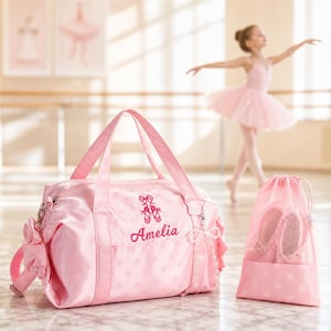 May include: A pink duffel bag with a white polka dot pattern, featuring an embroidered design of ballet slippers and the name Amelia in script. A matching pink drawstring mesh bag sits beside it, both accented with decorative ribbon details.