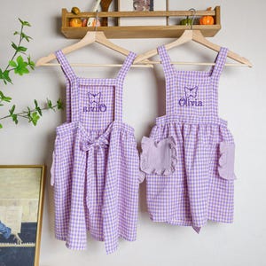 May include: Two purple and white gingham aprons with butterfly embroidery. One apron says "Olivia" and the other says "Olivia".