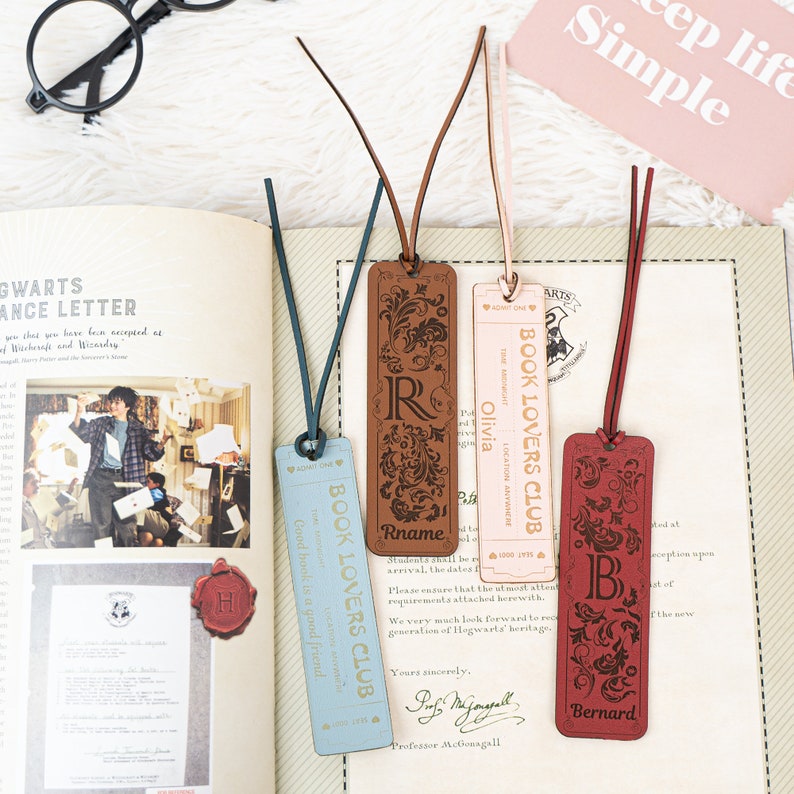 May include: Four leather bookmarks with decorative floral designs and personalized names. The bookmarks are in blue, brown, pink, and red. The text on the bookmarks reads "Book Lovers Club" and includes the names "Olivia", "Rname", "Bernard", and "Good hook is a good friend".