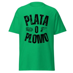以下が含まれることがあります： お金と銃のグラフィックが描かれた、黒い「PLATA O PLOMO」の文字が書かれた緑色のTシャツです。