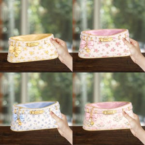 May include: Four floral-patterned cosmetic bags in yellow, pink, blue, and pink. Each bag has a gold-tone clasp, bow, and charm. The bags are rectangular with a curved top and are held by hands.