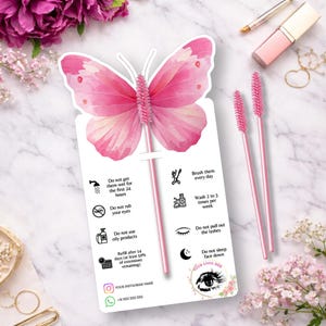 May include: A pink butterfly-shaped card with instructions for eyelash extensions. The card has a pink brush attached and is surrounded by beauty products and flowers. The card includes text such as "Do not get them wet for the first 24 hours."