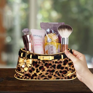 May include: A leopard print cosmetic bag filled with beauty products, including a perfume bottle, hand cream, a makeup brush, and wrapped chocolates. The bag has a gold zipper and bow detail.