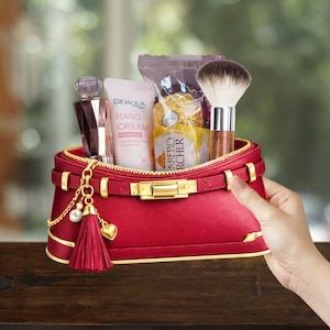 May include: A red cosmetic bag with gold accents, filled with beauty products. The bag contains a perfume bottle, hand cream, a makeup brush, and wrapped chocolates. A gold chain with a tassel and heart charm hangs from the bag.