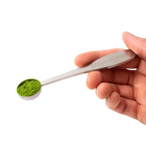 May include: A stainless steel matcha spoon holds a scoop of bright green matcha powder. The spoon has a long, flat handle with the brand name "CHAZERU" etched on it. The spoon is held in a person's hand against a white background.