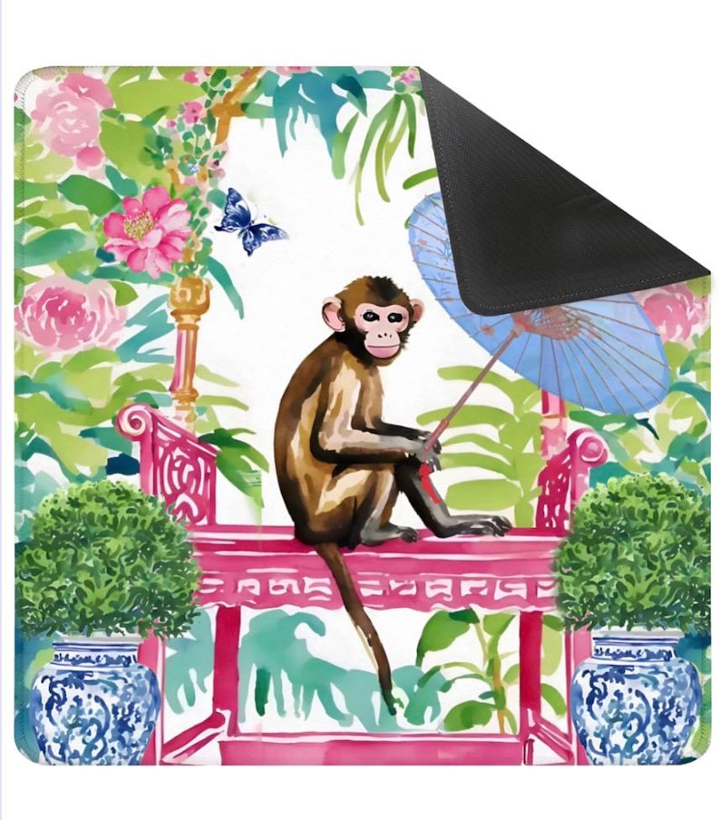 K&ouml;nnte beinhalten: Dekorative Matte mit einer Aquarellillustration eines Affen, der auf einer rosa Bank sitzt und einen blauen Sonnenschirm h&auml;lt. Der Hintergrund umfasst rosa Blumen, gr&uuml;nes Laub und einen blauen Schmetterling. Zwei blau-wei&szlig;e Vasen flankieren die Bank.
