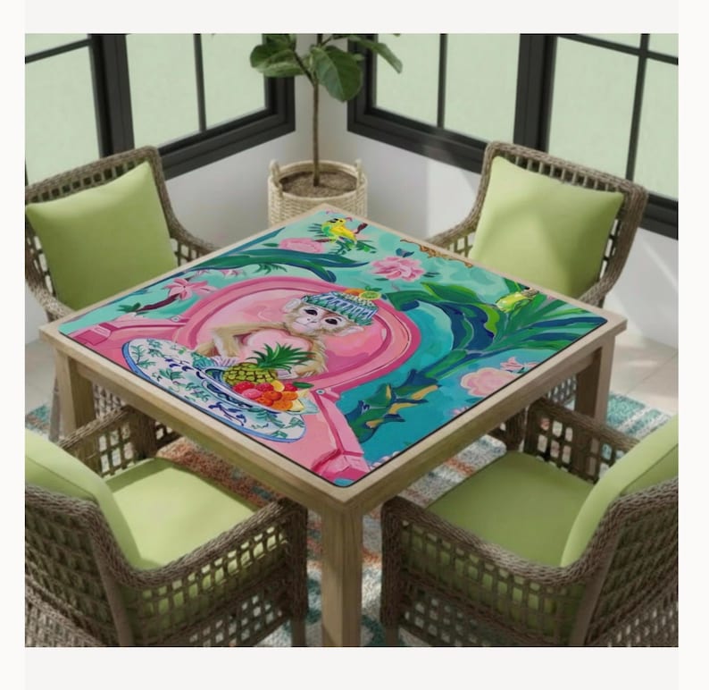 May include: A square wooden table with a colorful, tropical-themed tabletop featuring a monkey, flowers, and fruit. The table is surrounded by four wicker chairs with green cushions, creating a vibrant outdoor dining set.