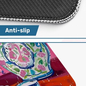 Op de afbeelding: Close-up van een zwarte antislipmat met witte stiksels. Het onderste gedeelte toont een kleurrijk, waterdicht ontwerp met een bloemenpatroon op een blauw-witte vaas, kopjes en borden.
