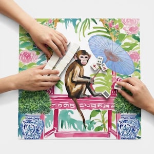 K&ouml;nnte beinhalten: Bunte Illustration eines Affen, der Mahjong spielt. Der Affe ist braun und sitzt auf einer rosa Struktur mit floralem und laubartigem Hintergrund. Ein blauer Sonnenschirm und blau-wei&szlig;e Vasen sind ebenfalls zu sehen.