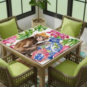May include: Square wooden table with a decorative top featuring a watercolor illustration of a monkey wearing a straw hat, surrounded by flowers and vases. The table is surrounded by four wicker chairs with green cushions.