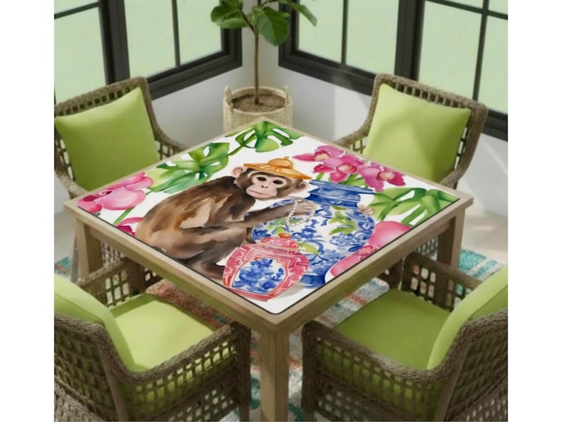 May include: Square wooden table with a decorative top featuring a watercolor illustration of a monkey wearing a straw hat, surrounded by flowers and vases. The table is surrounded by four wicker chairs with green cushions.