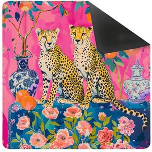 Pode incluir: Tapete decorativo com dois guepardos com manchas amarelas e pretas, sentados sobre uma superfície com padrão floral azul. O fundo é rosa vibrante com ramos de laranjeiras e vasos decorativos. O tapete tem uma parte inferior preta.