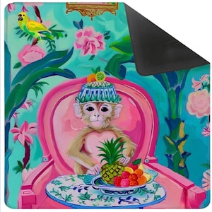 May include: A colorful decorative mat featuring a monkey in a hat seated in a pink chair, with a pineapple and fruit on a table. The background has a floral and tropical design with a parrot. The mat has a black backing.