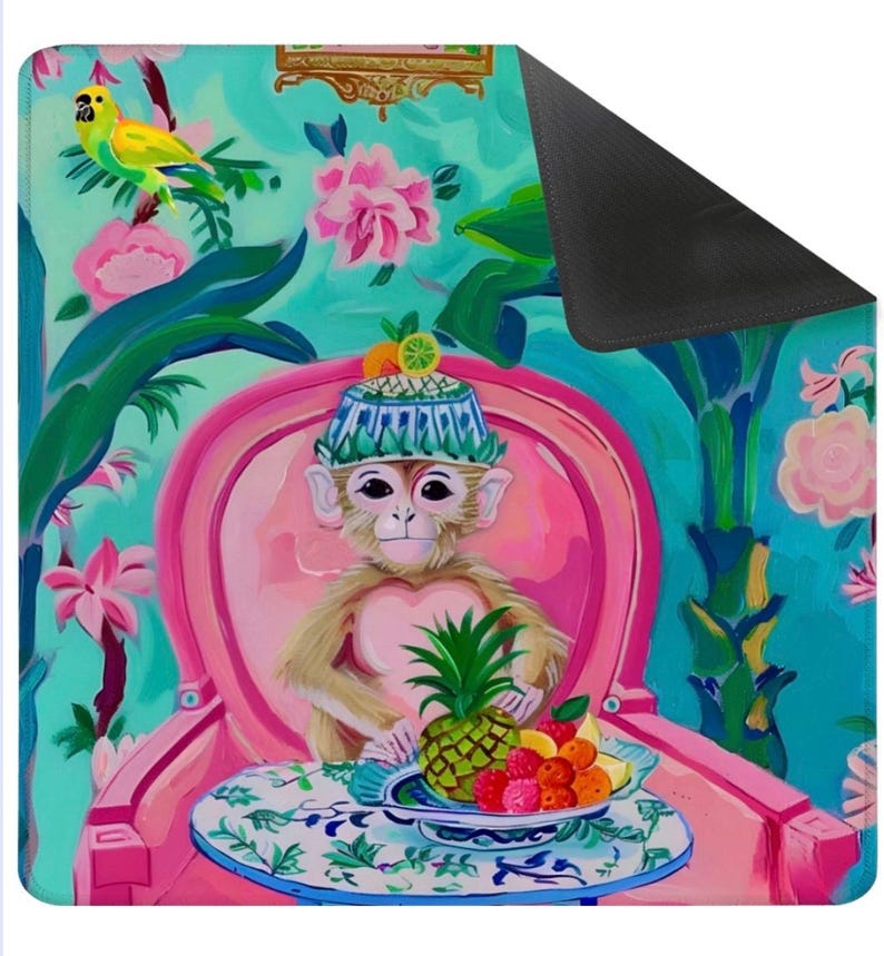 May include: A colorful decorative mat featuring a monkey in a hat seated in a pink chair, with a pineapple and fruit on a table. The background has a floral and tropical design with a parrot. The mat has a black backing.