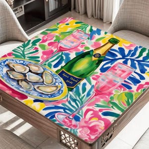 K&ouml;nnte beinhalten: Ein quadratischer Holztisch mit einem farbenfrohen Blumenmuster. Auf dem Tisch befinden sich eine Champagnerflasche, zwei Sektgl&auml;ser und ein Teller mit Austern. Der Tisch ist von zwei St&uuml;hlen umgeben.