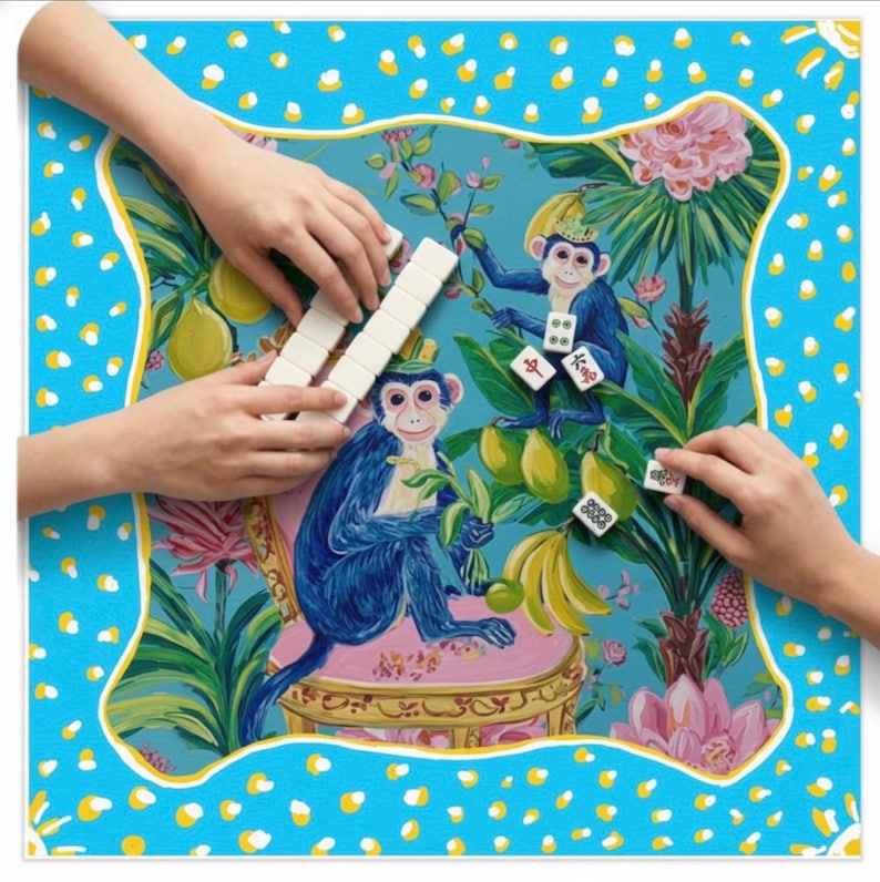 May include: A vibrant Mahjong game set with a playful design. The game board has a blue background with a monkey illustration, a yellow border, and white polka dots. Hands are shown playing the game with white tiles.