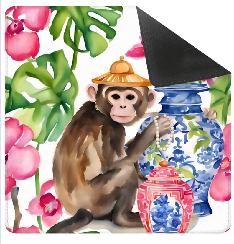 May include: A decorative mat featuring a watercolor illustration of a monkey wearing a straw hat, holding a pearl necklace, and surrounded by pink flowers, green leaves, and blue and white vases. The mat has a black backing.