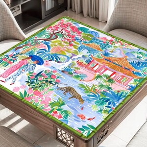 May include: A square wooden table featuring a detailed, colourful illustration on the tabletop. The artwork shows figures, a leopard, and Asian-inspired architecture. The table is surrounded by four chairs.