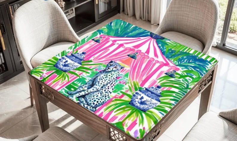 Puede incluir: Un mantel cuadrado con un patr&oacute;n vibrante de un guepardo, tarros de jengibre azules y blancos, y hojas de palma verdes sobre un fondo de rayas verticales de color rosa brillante y blanco. El dise&ntilde;o es colorido, detallado y gr&aacute;fico.