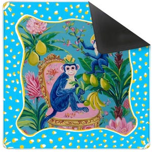 May include: A decorative mat with a vibrant illustration of blue monkeys in a tropical setting, with pink flowers, yellow fruit, and a pink chair. The mat has a blue border with white and yellow polka dots and a black underside.