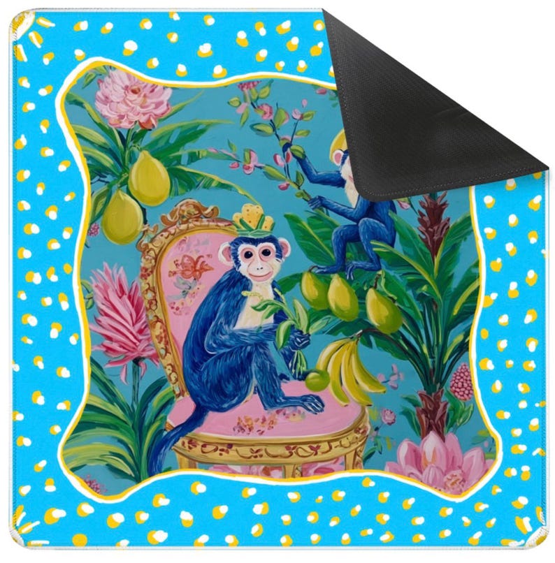 May include: A decorative mat with a vibrant illustration of blue monkeys in a tropical setting, with pink flowers, yellow fruit, and a pink chair. The mat has a blue border with white and yellow polka dots and a black underside.