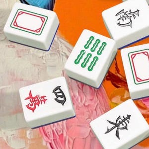 May include: White Mahjong tiles with red, green, and black symbols and designs are scattered on a colorful background. The tiles feature various symbols and patterns, including rectangles, lines, and Chinese characters. The game pieces are arranged in a visually appealing manner.