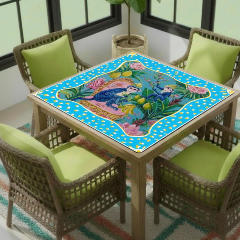 May include: A square wooden table with a blue patterned table cover featuring two blue monkeys, flowers, and fruit. The table is surrounded by four wicker chairs with green cushions. The table is set on a striped rug.