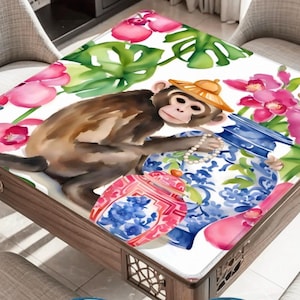 May include: A decorative table with a watercolor design featuring a monkey wearing a hat, surrounded by pink orchids, green leaves, and blue and red patterned vases. The table is made of wood.