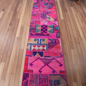 May include: A long, rectangular runner rug featuring a vibrant patchwork design. The rug is composed of various sections in shades of hot pink, magenta, purple, orange, and teal, displaying a mix of geometric patterns, diamonds, and linear motifs.