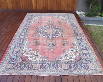 May include: A rectangular area rug featuring a large central medallion in dark blue and cream on a faded coral pink background. The rug has a wide, intricate border with floral and geometric patterns in shades of blue, cream, and muted green.