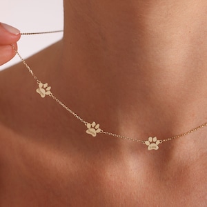 May include: Gold necklace with three paw print charms, each engraved with a different name: "Boomer", "Amelia", and "Lola".