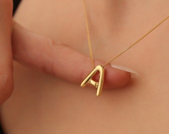May include: A gold necklace with a simple, abstract letter A pendant.