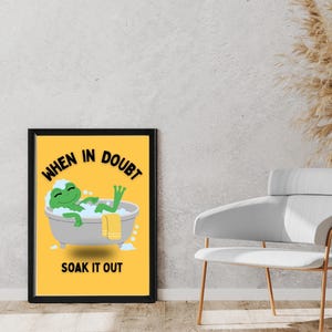 Puede incluir: Un póster enmarcado con fondo amarillo, que presenta una rana de dibujos animados en una bañera. El texto "WHEN IN DOUBT SOAK IT OUT" se muestra en blanco y negro. El póster está en un marco negro.
