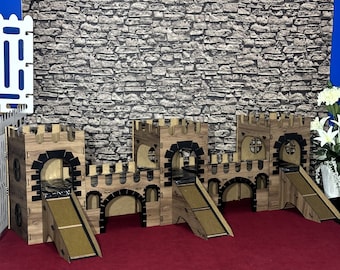 May include: A cardboard play structure for small animals, designed to look like a medieval castle. It has three towers with arched doorways and a ramp leading up to the top. The structure is made of brown cardboard and has black accents.