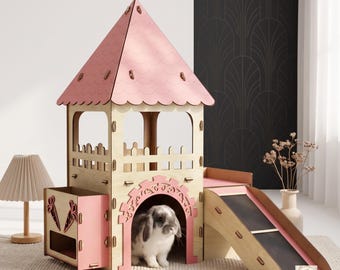 Puede incluir: Un castillo de madera para mascotas con acabado en madera clara y detalles en rosa, que presenta un techo puntiagudo, un balcón con valla, una rampa lateral y una entrada arqueada. Un pequeño conejo gris y blanco está dentro de la estructura.