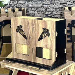 Könnte beinhalten: Eine Holzkiste mit zwei Fächern, jedes mit einem Ausschnitt in Form einer Karotte. Die Kiste ist an den Seiten schwarz und hat unten ein Holzregal.