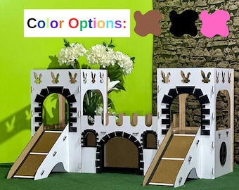 Puede incluir: Una estructura de juego de madera blanca y negra con temática de castillo con dos toboganes y entradas arqueadas. La estructura tiene siluetas de conejos recortadas y el texto "Color Options:" encima de tres muestras de color: marrón, negro y rosa.