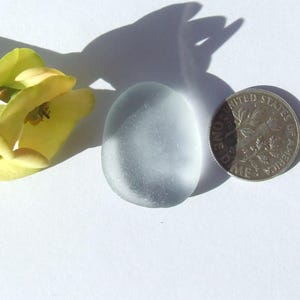 Puede incluir: Una piedra de vidrio de mar lisa de color azul claro, junto a una flor amarilla y una moneda de EE. UU. con el texto "UNITED STATES OF AMERICA" y "ONE CENT".