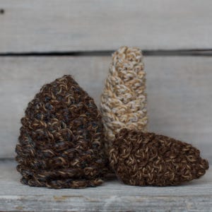 May include: Three crocheted hats in brown, beige, and cream colors. The hats are made with a textured stitch and have a rounded shape.