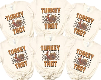 May include: Six cream-colored t-shirts with the words "TURKEY TROT" in brown, featuring a cartoon turkey on a checkered background. The shirts are knotted at the bottom.