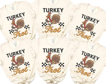 Peut inclure: Six t-shirts crème avec l'inscription "TURKEY Trot" et une illustration d'une dinde de dessin animé portant un dossard "2025". La dinde court sur un motif de drapeau à damier. Le texte et le graphisme sont en marron, orange et noir.