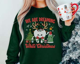 May include: Green Christmas sweatshirt with a white tooth wearing a red bow and reindeer antlers. The tooth is holding a tube of toothpaste and a toothbrush. The text on the sweatshirt reads "We are dreaming of a White Christmas".