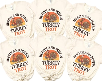 May include: Six cream-colored t-shirts with the text "HUFFIN AND PUFFIN TURKEY TROT" in a circular design. The design includes a cartoon turkey running across a sunset background. The year "2025" is printed on the turkey.